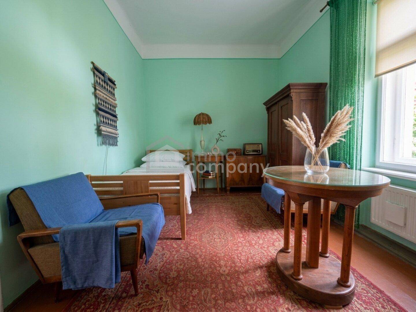 Schlafzimmer mit Einzelbett, Holzmöbeln, blauem Sessel und grünen Wänden, das einen traditionellen Charme besitzt.