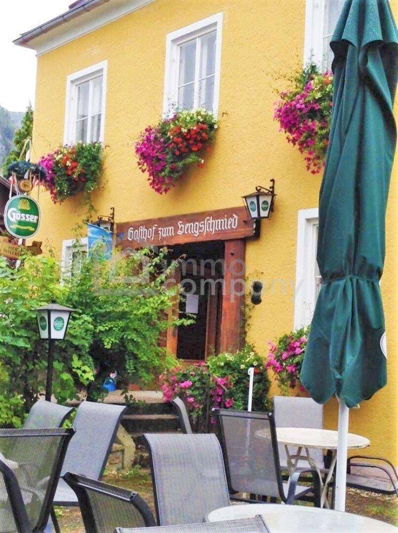Gelbe Fassade eines Gasthofs mit blühenden Blumenkästen und einem gemütlichen Außenbereich mit Sonnenschirm.