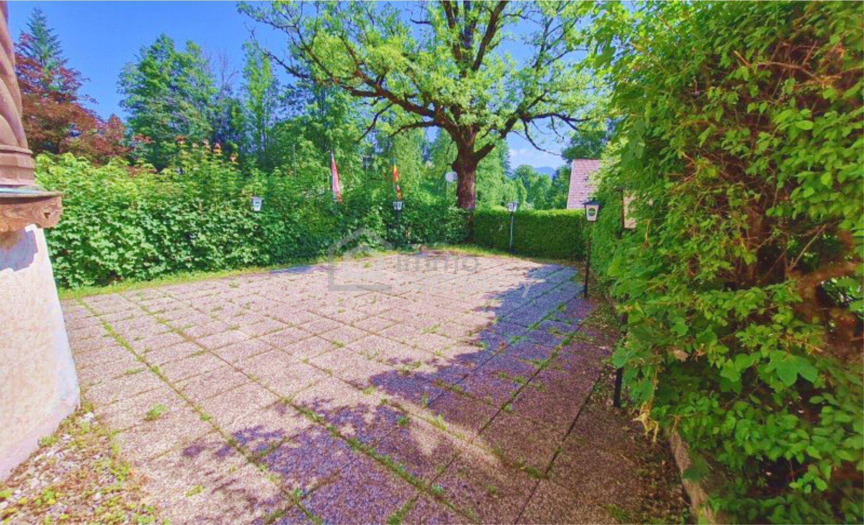 Gepflasterter Außenbereich umgeben von üppigem Grün und Bäumen an einem sonnigen Tag.
