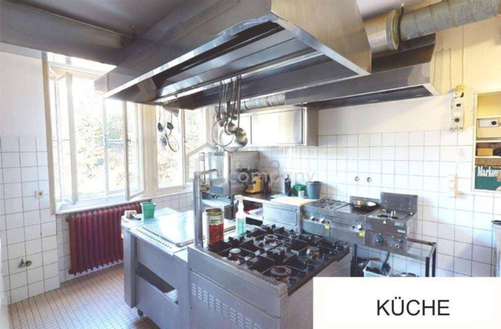 Große Gewerbeküche mit professionellen Edelstahlgeräten und Fliesen an den Wänden.