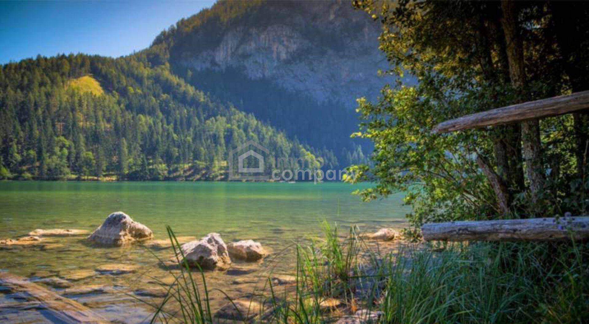 Malerischer Blick auf einen klaren Bergsee umgeben von bewaldeten Hängen und Felsen.