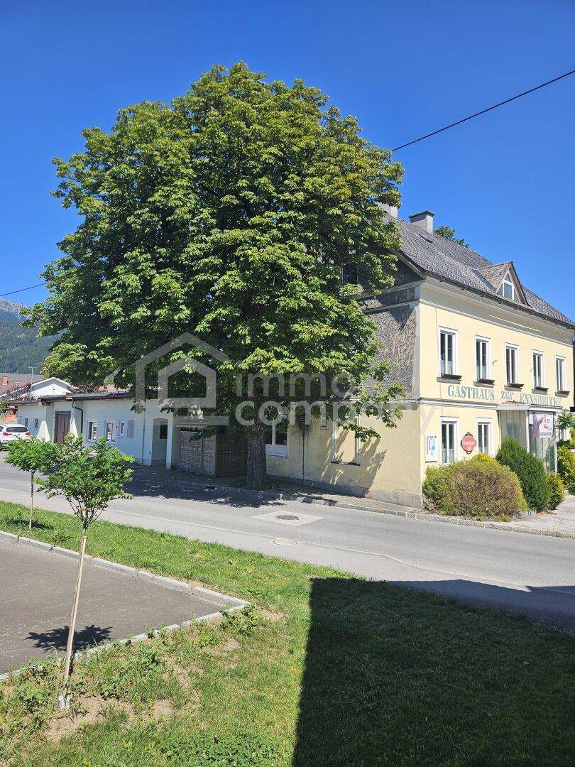 Seitenansicht des gelben Gasthauses mit einem großen Baum und einem weiteren Gebäude im Hintergrund.