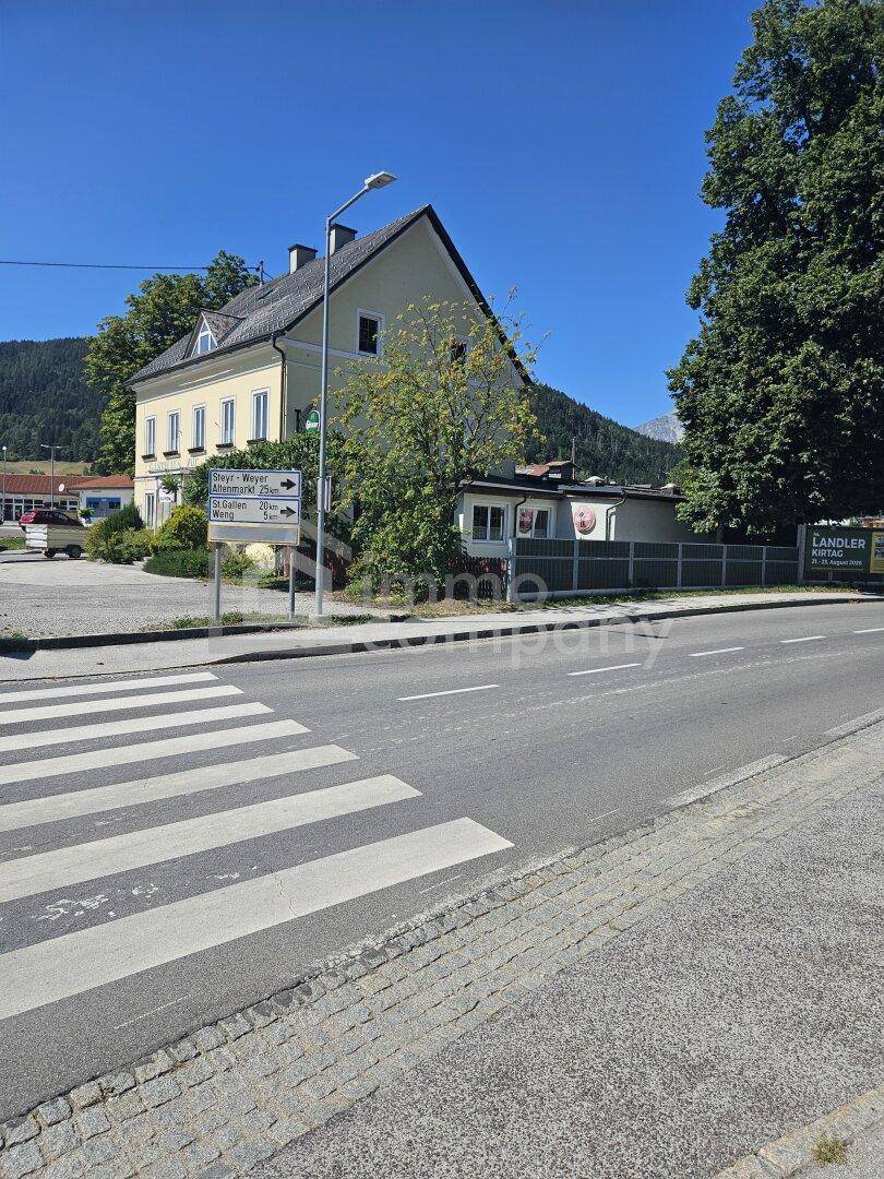 Straßenansicht mit Zebrastreifen im Vordergrund und dem gelben Gebäude mit Bergen im Hintergrund.