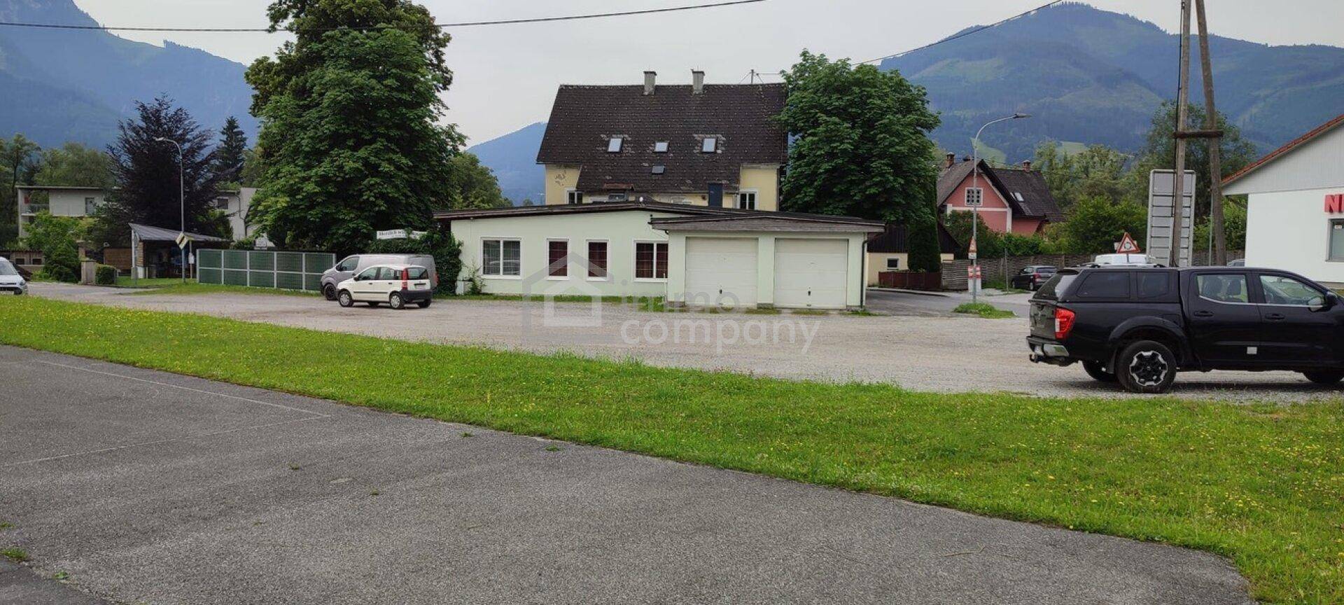 Weitläufige Ansicht mit dem gelben Gebäude, einem kleineren Gebäude mit Garagen und einem Parkplatz.