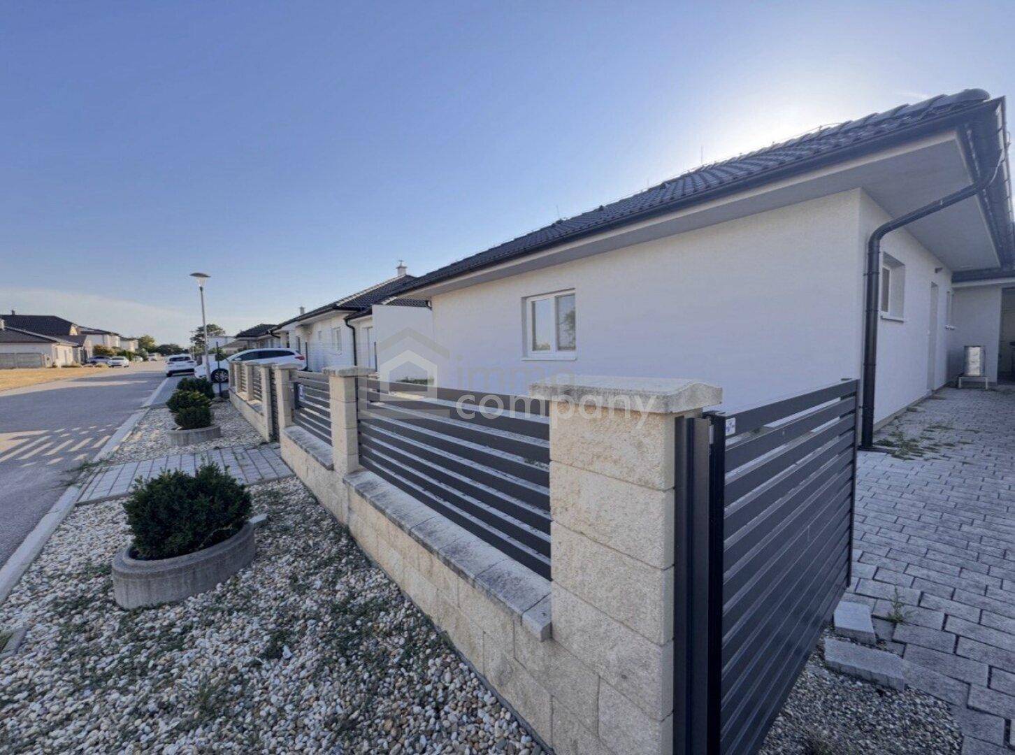 Seitenansicht eines modernen Hauses mit Zaun und gepflastertem Gehweg an einem sonnigen Tag.