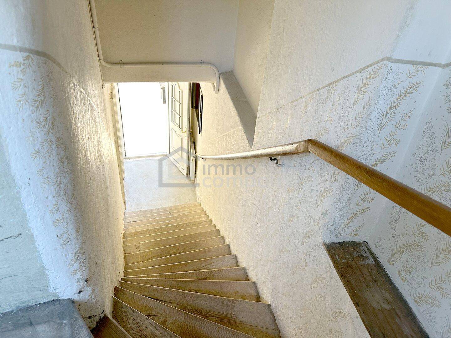 Helle Holztreppe mit Handlauf und gemusterten Wänden, die in einen unteren Bereich führt.