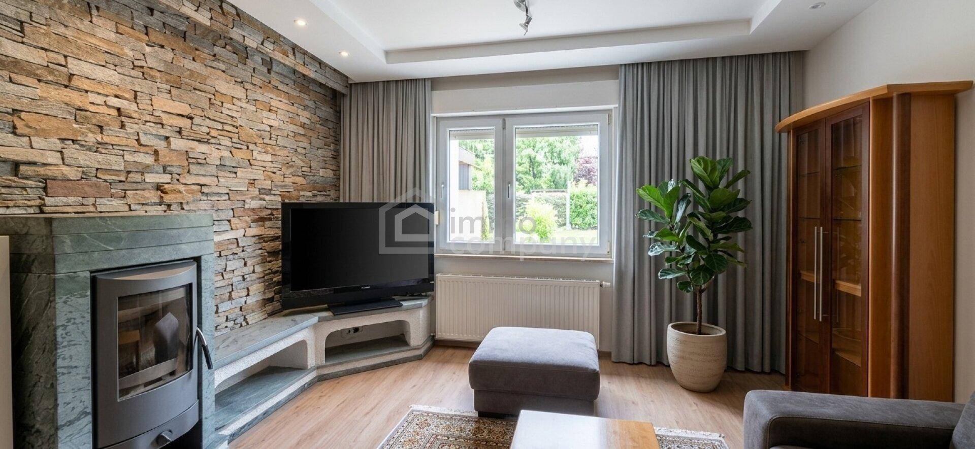 Gemütliches Wohnzimmer mit Kamin, Steinwand und Blick in den grünen Garten.