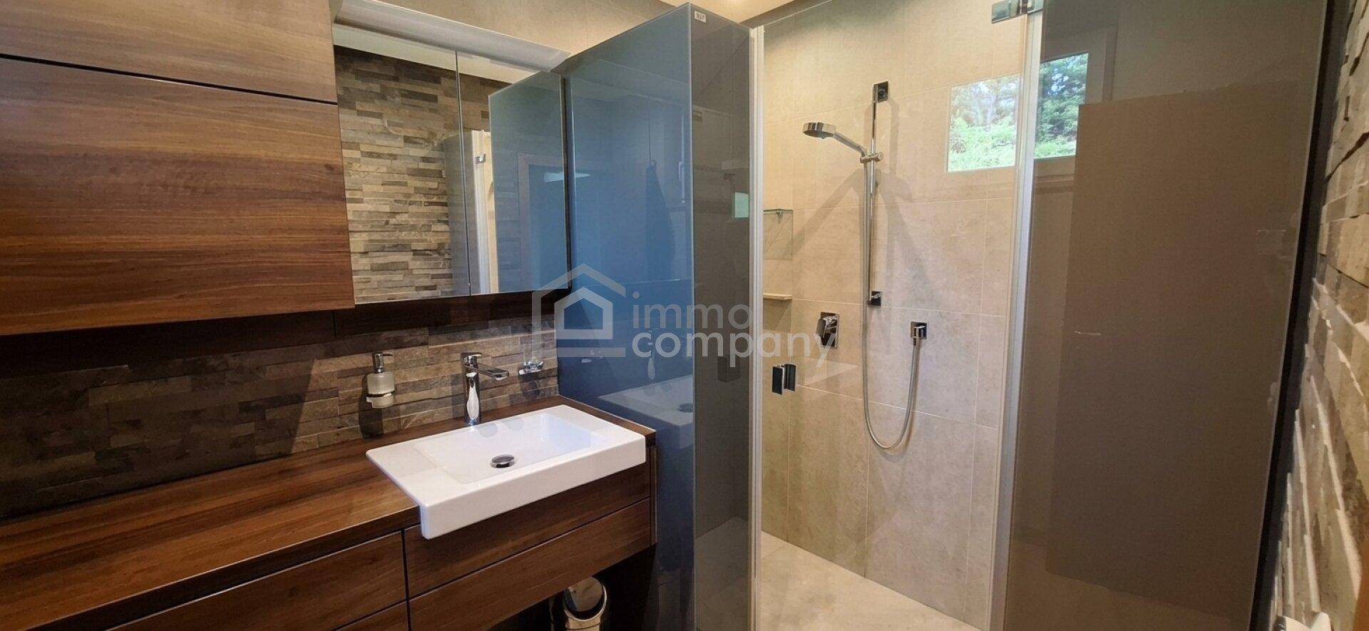 Modernes Badezimmer mit begehbarer Dusche, Holzwaschtisch und Steinwandakzenten.