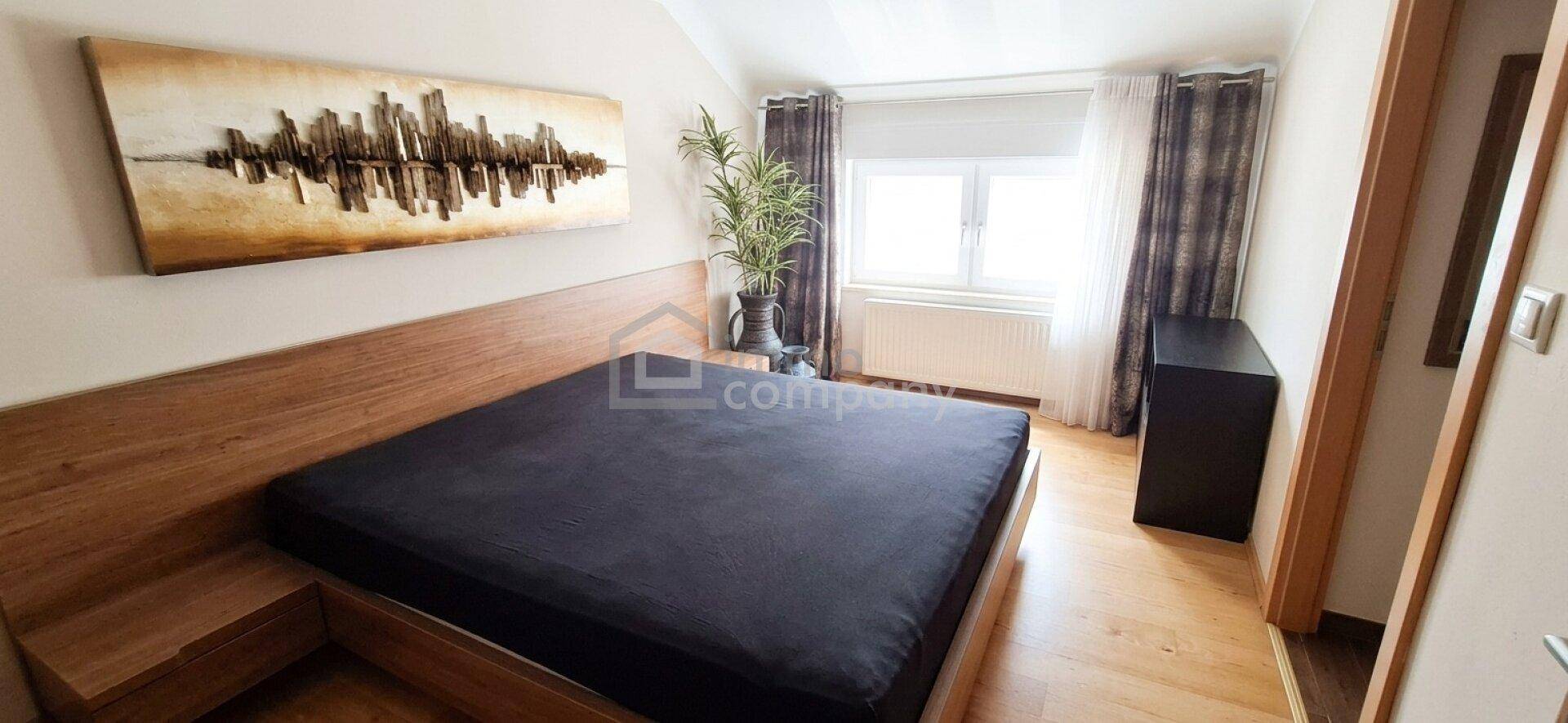 Helles Schlafzimmer mit Holzbett, Parkettboden und modernem Wandbild.