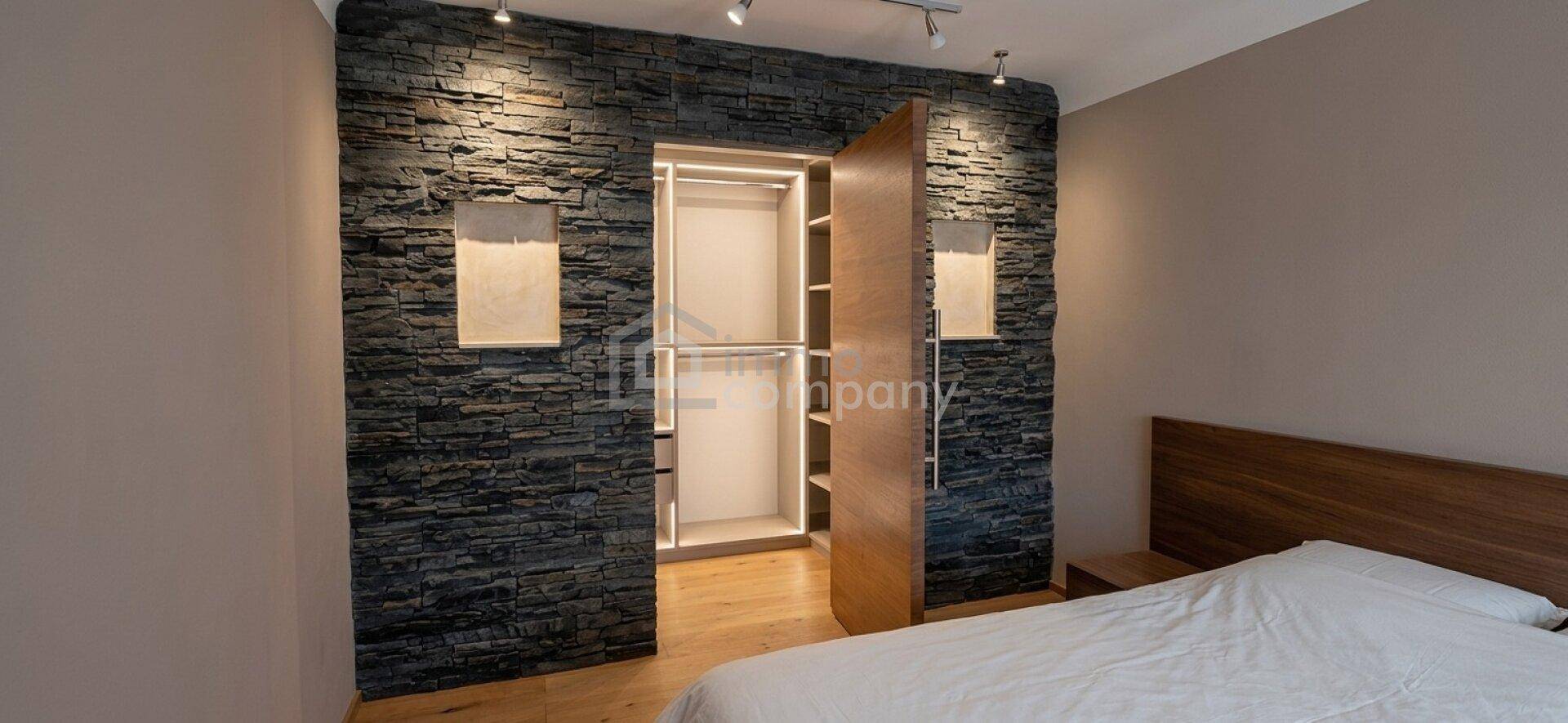 Schlafzimmer mit integriertem Kleiderschrank, Steinwand und Holzboden.