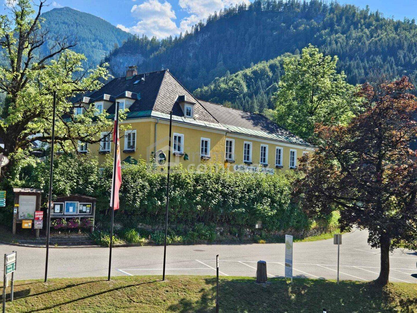 Historisches gelbes Gebäude mit Mansarddach, eingebettet in eine grüne Berglandschaft unter strahlend blauem Himmel.