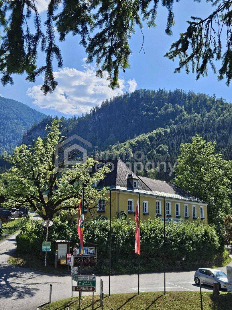 Malerisches gelbes Haus mit traditioneller Architektur, umgeben von üppiger Natur und hohen Bergen.