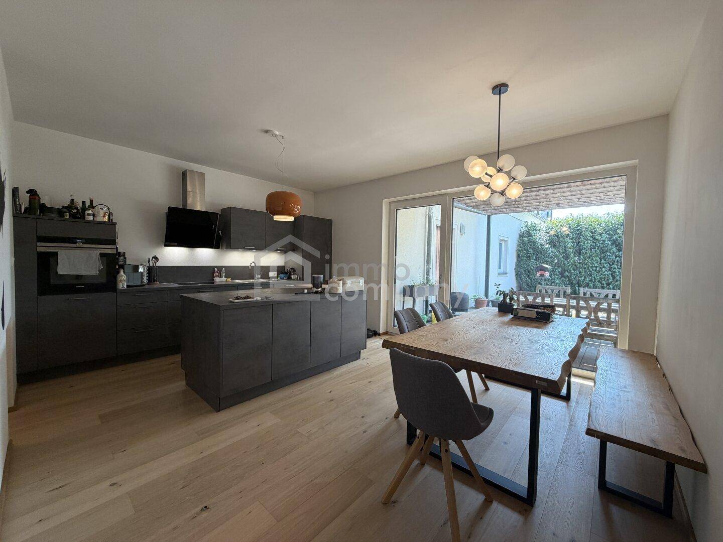 Moderne offene Küche mit Kücheninsel, Essbereich und Zugang zu einer Terrasse im Freien.