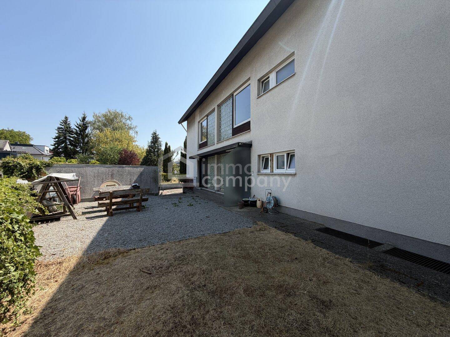 Seitenansicht des Hauses mit Kiesfläche, trockenem Rasen und einem Picknicktisch im Freien.