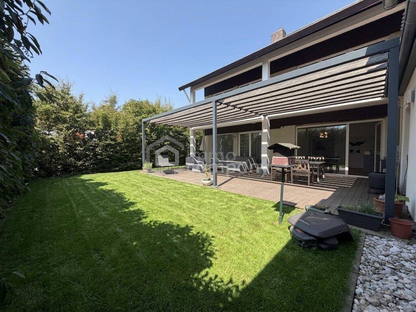 Gepflegter Garten mit Rasenfläche und einer überdachten Terrasse, ideal für entspannte Stunden im Freien.