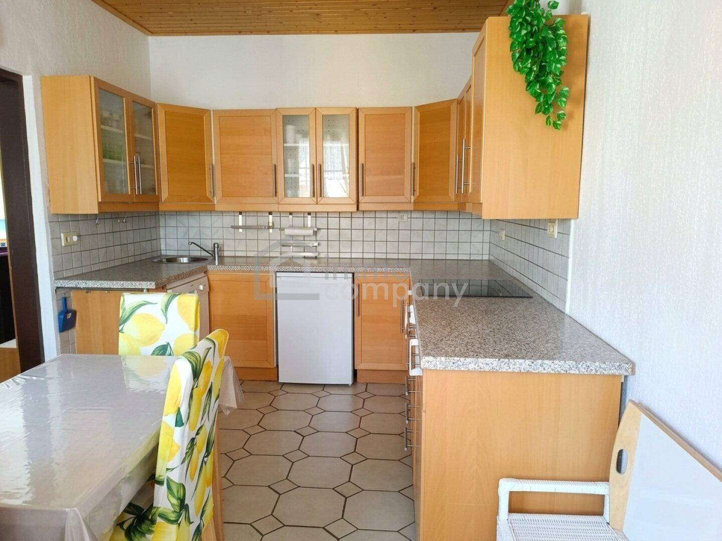 Helle Küche mit Holzschränken, Granitarbeitsplatte und gefliestem Boden, inklusive Essbereich.