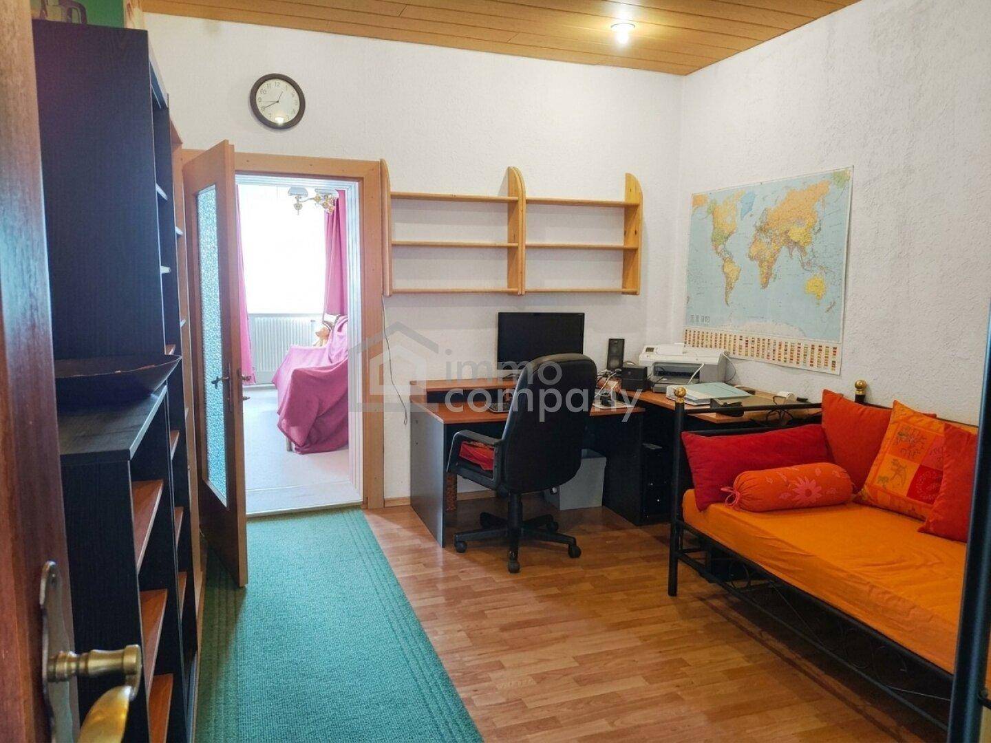 Arbeitszimmer mit Schreibtisch, Regal und Tagesbett, mit Blick in ein angrenzendes Zimmer.