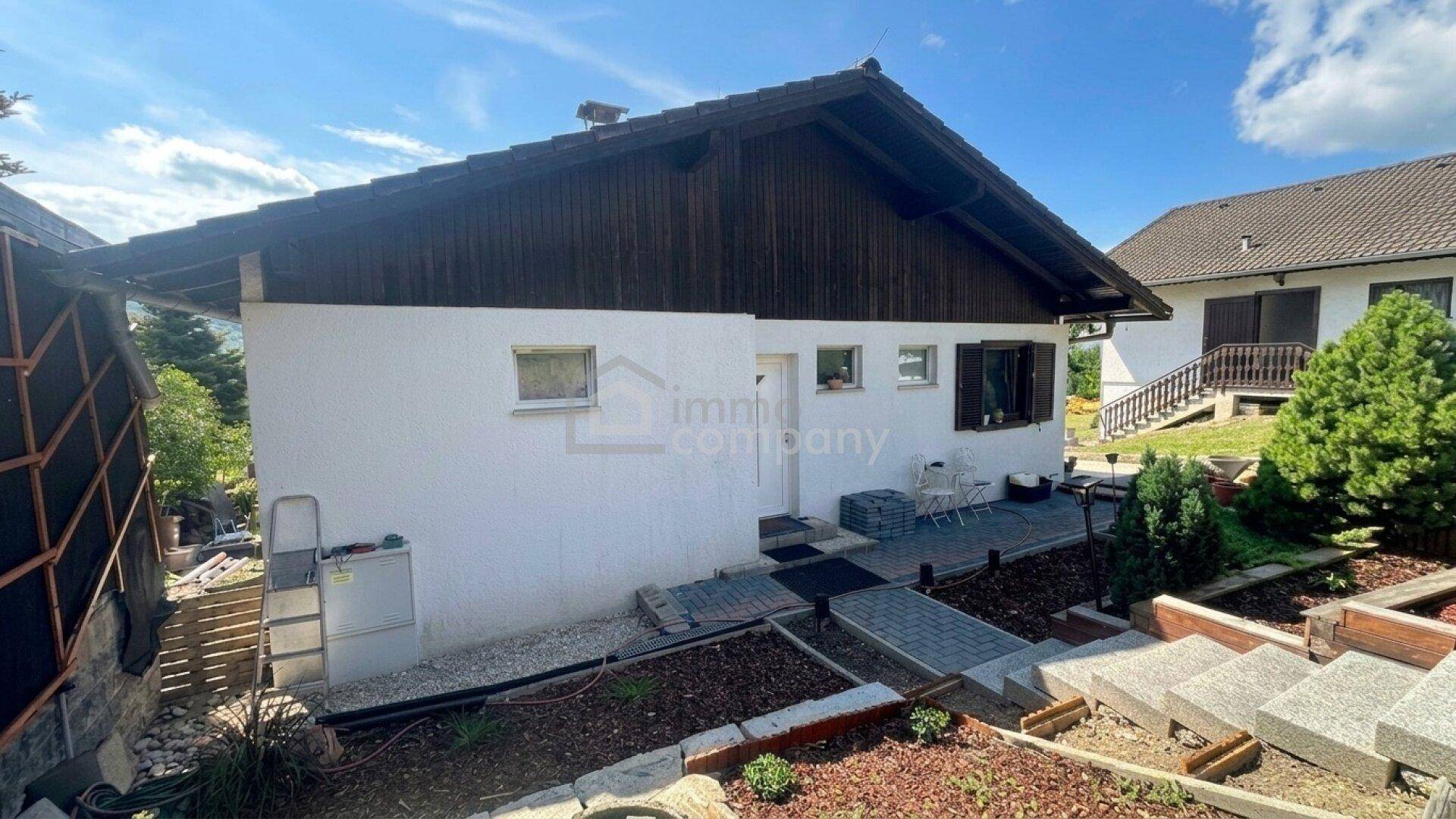 Seitenansicht des Hauses mit weißer Fassade, Holzelementen und einem kleinen Gartenbereich.