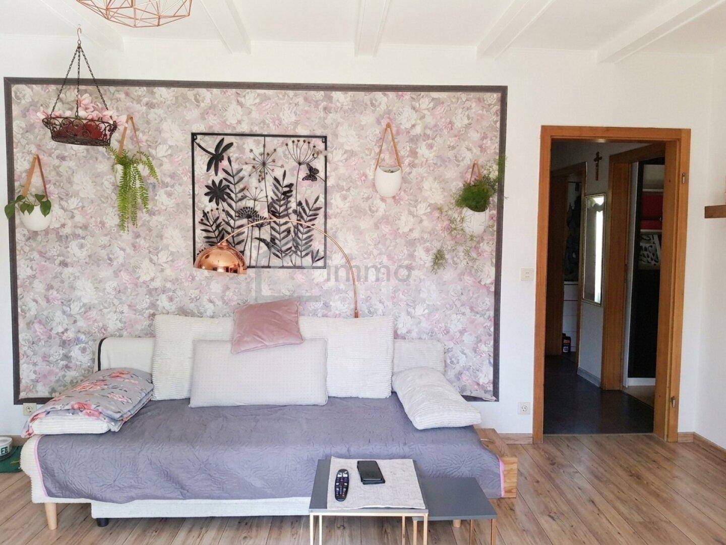 Helles Wohnzimmer mit Tagesbett, floraler Tapete und dekorativen Hängepflanzen.