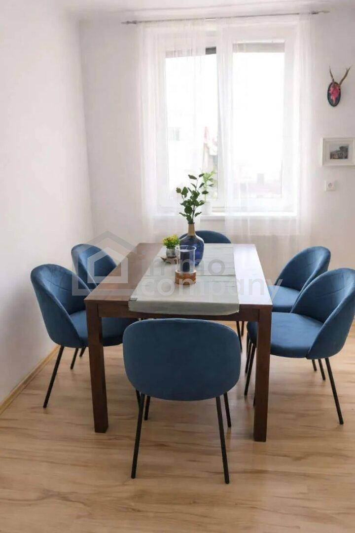 Essbereich mit Holztisch und sechs blauen Samtstühlen, beleuchtet durch ein großes Fenster.