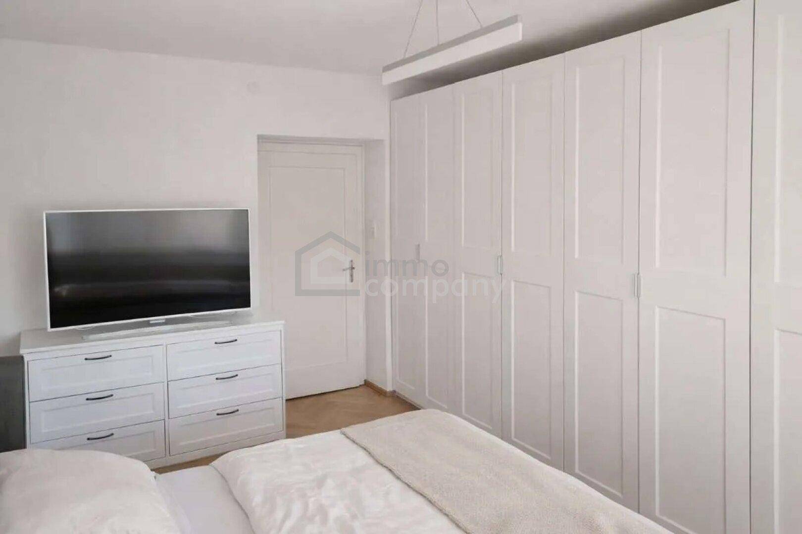 Schlafzimmer mit großen weißen Einbauschränken und einem Fernseher auf einer Kommode.