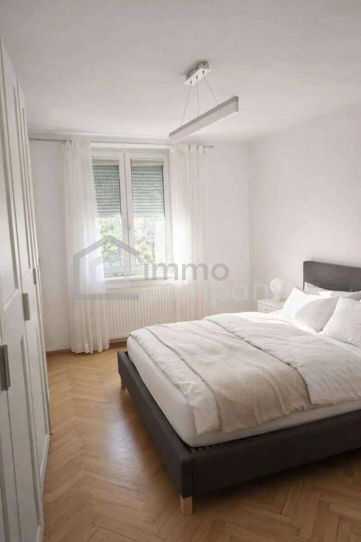 Helles Schlafzimmer mit Doppelbett, Holzboden und großem Fenster mit Blick ins Grüne.