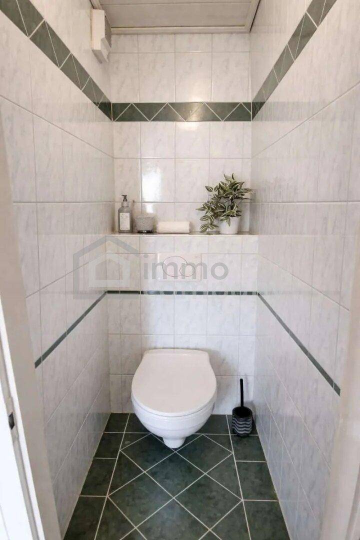 Separate Toilette mit weißen und grünen Fliesen, Wand-WC und kleiner Ablagefläche.