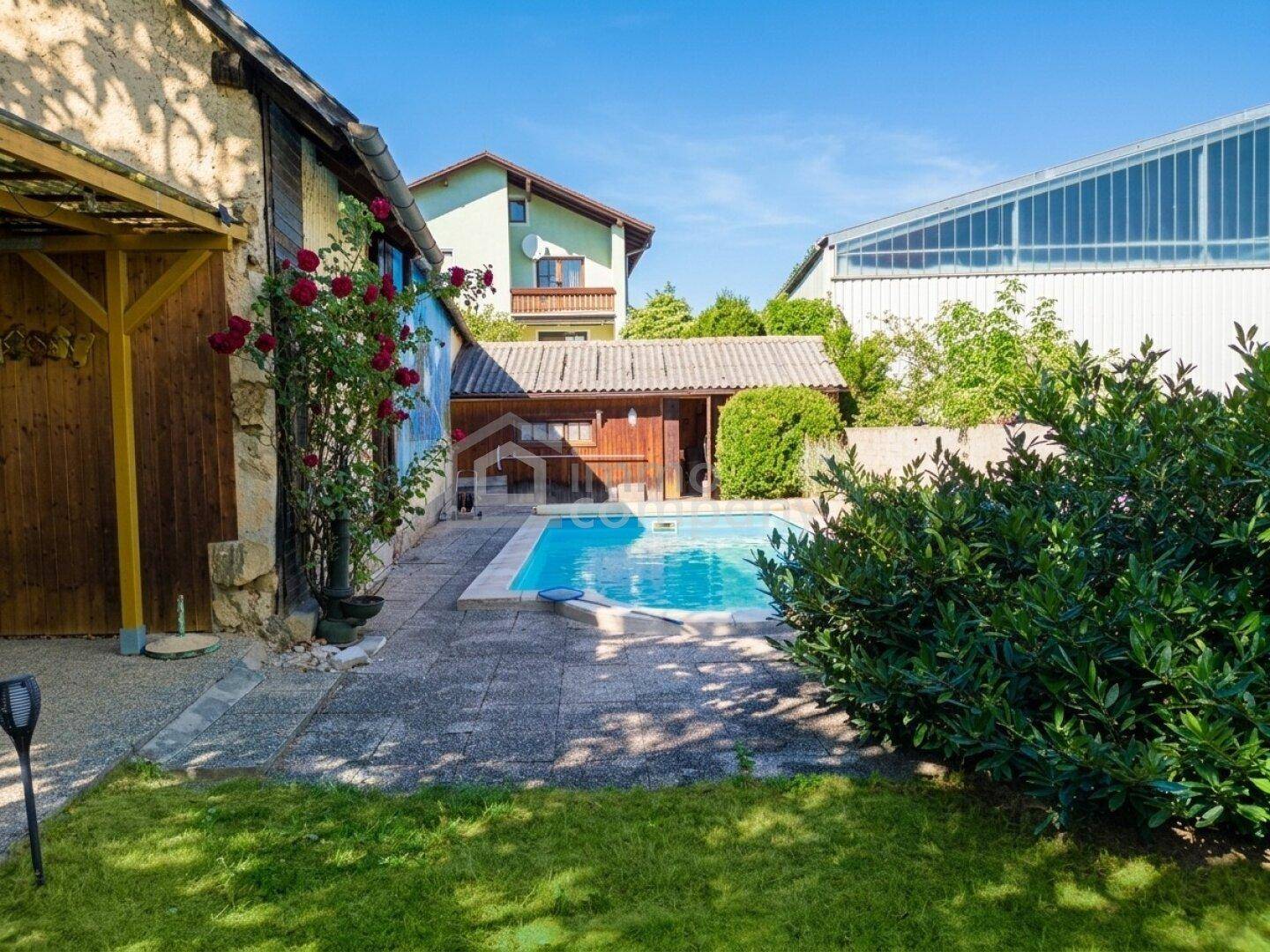 Garten mit Swimmingpool, gepflasterter Fläche und umgebenden Büschen unter blauem Himmel.