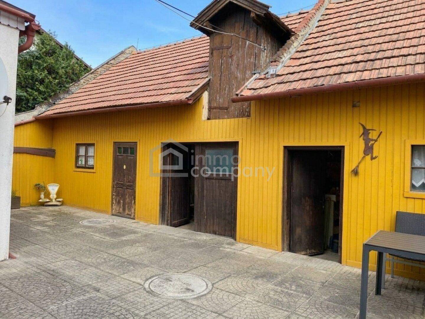Gelbes Nebengebäude mit Holztüren und gepflastertem Hofbereich, typisch für ländliche Anwesen.