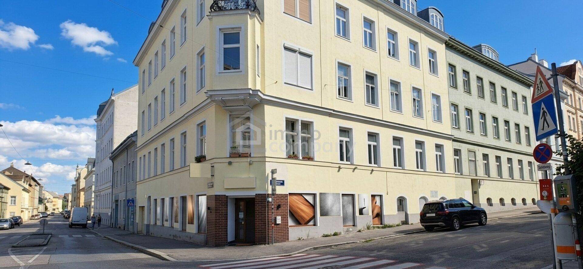 Historisches Eckgebäude mit einer hellgelben Fassade und vielen Fenstern, gelegen an einer belebten Stadtstraße.