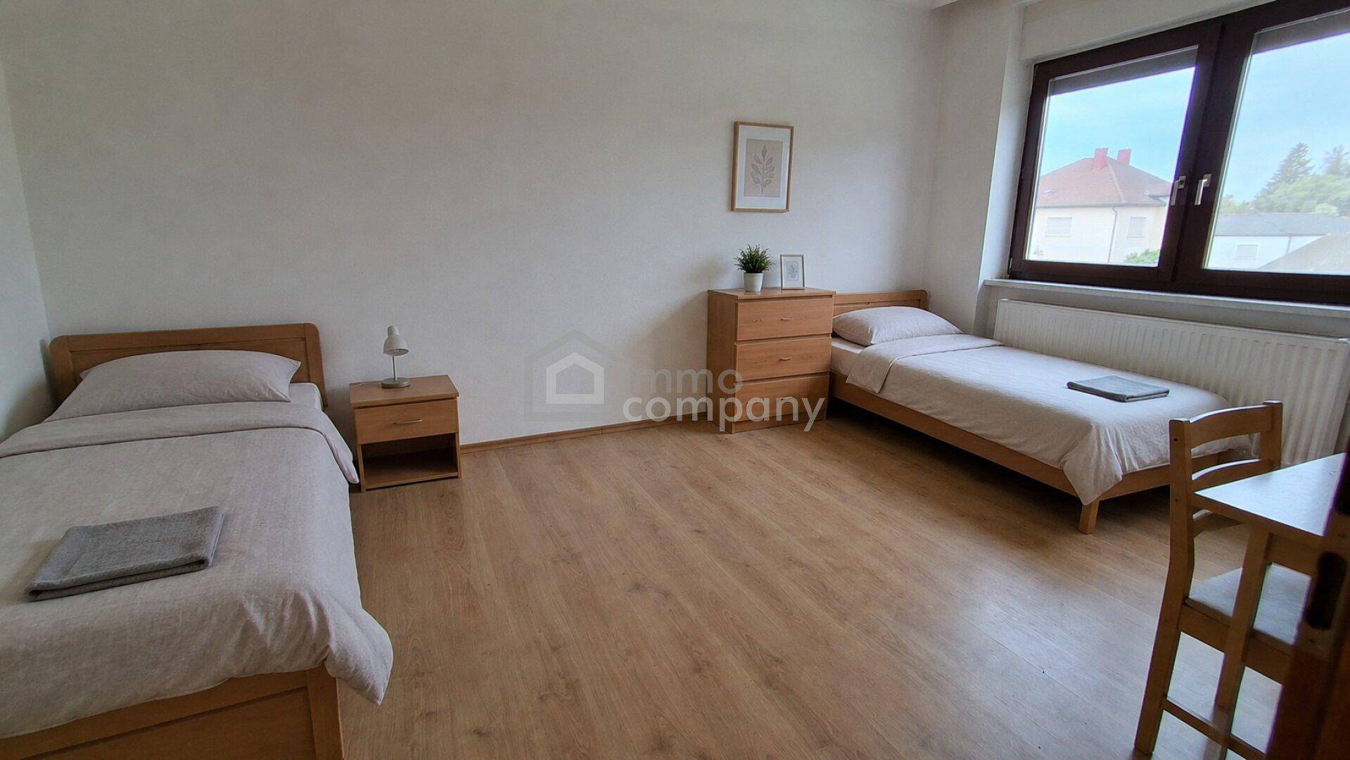 Geräumiges Schlafzimmer mit zwei Einzelbetten, Holzboden und großem Fenster mit Blick ins Grüne.