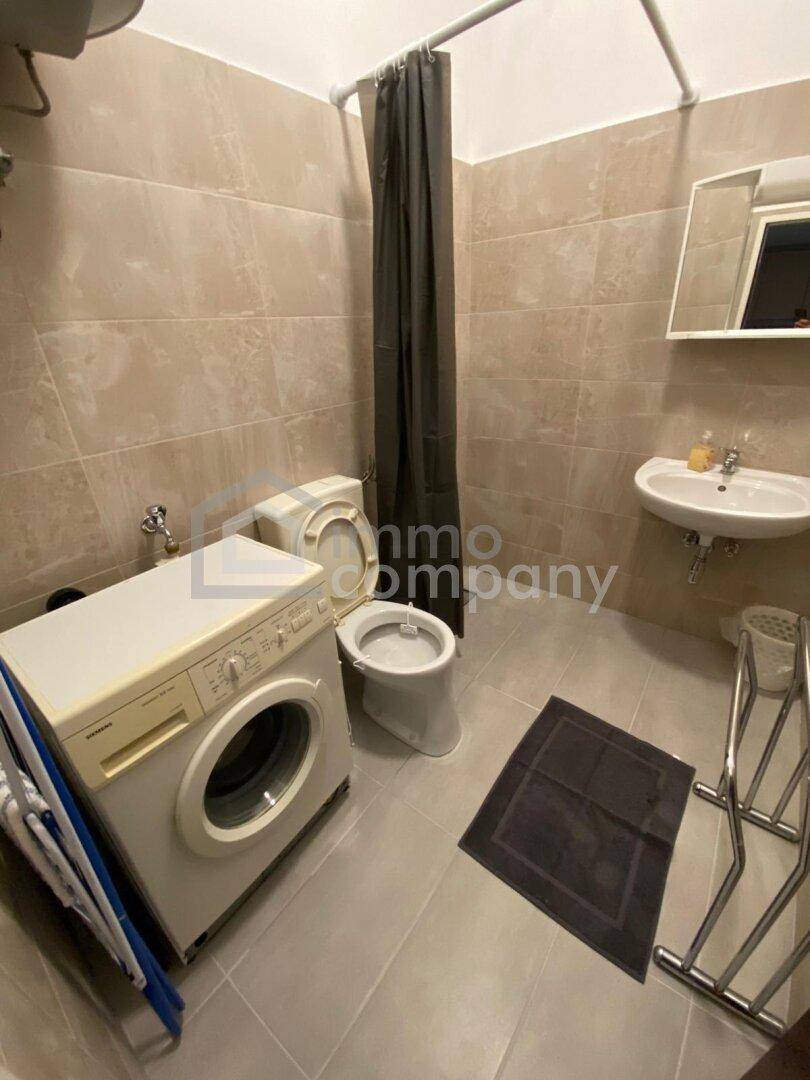 Funktionales Badezimmer mit Waschmaschine, WC, Waschbecken und Duschbereich.