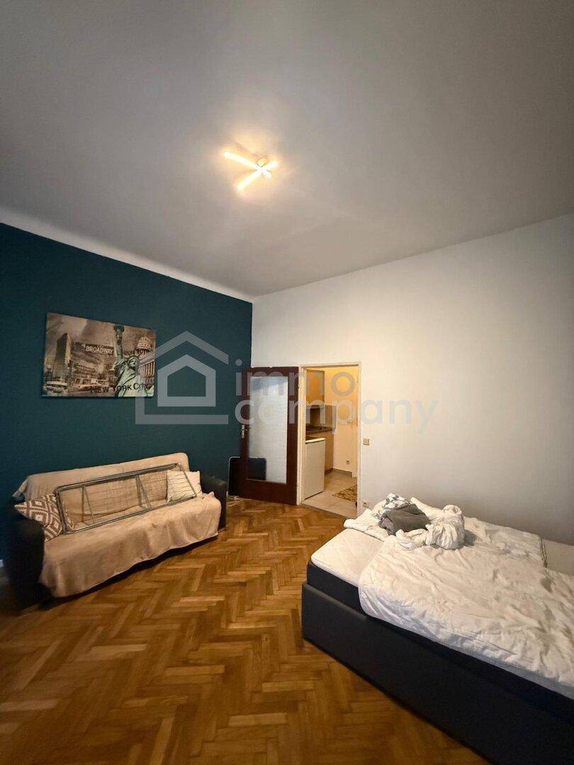 Gemütliches Schlafzimmer mit Parkettboden, Sofa und einer farbigen Akzentwand.