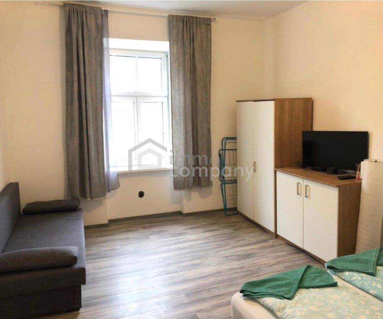 Helles Schlafzimmer mit großem Fenster, Sofa, Doppelbett und Laminatboden.