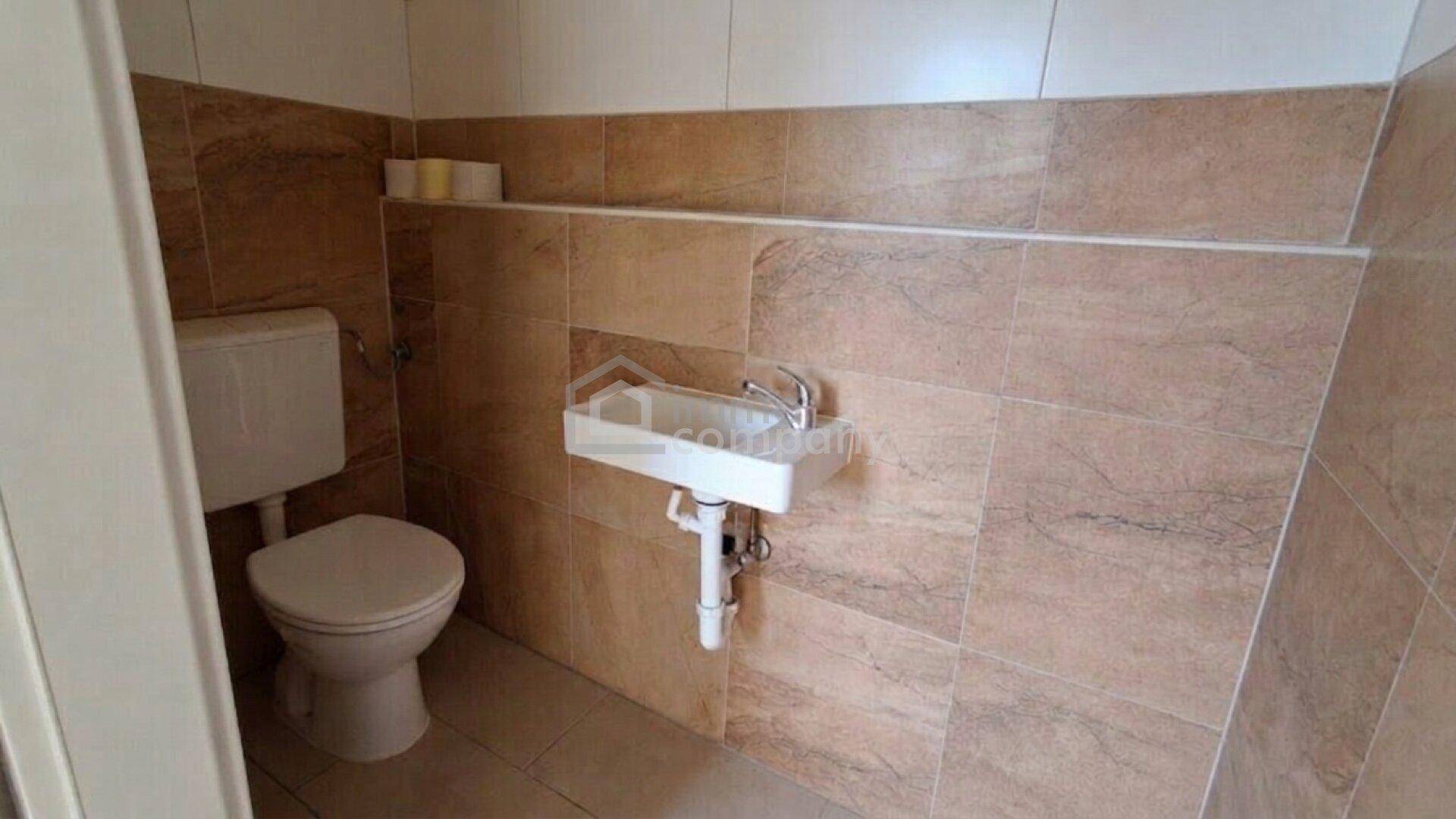 Kleines WC mit Wandfliesen und einfacher Toilette und Waschbecken.