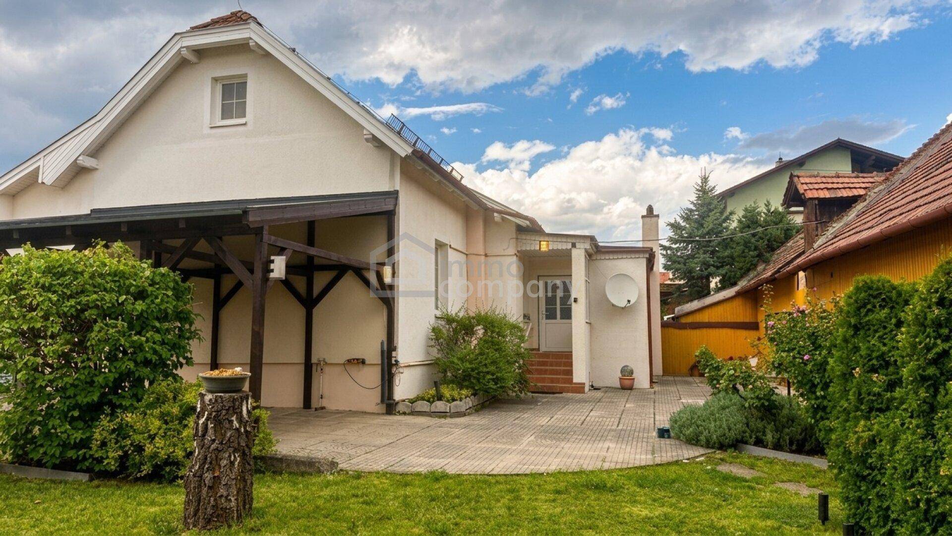 Hinteransicht des Hauses mit gepflasterter Terrasse und grünem Gartenbereich unter bewölktem Himmel.