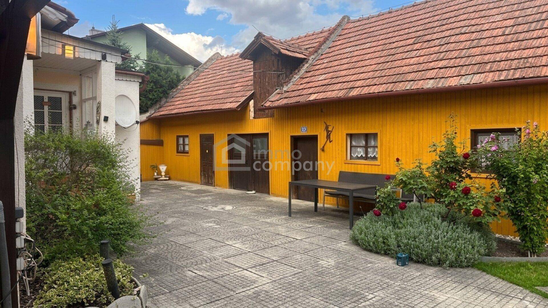 Gelbes Haus mit gepflastertem Innenhof und Sitzgelegenheiten im Freien, umgeben von Pflanzen.