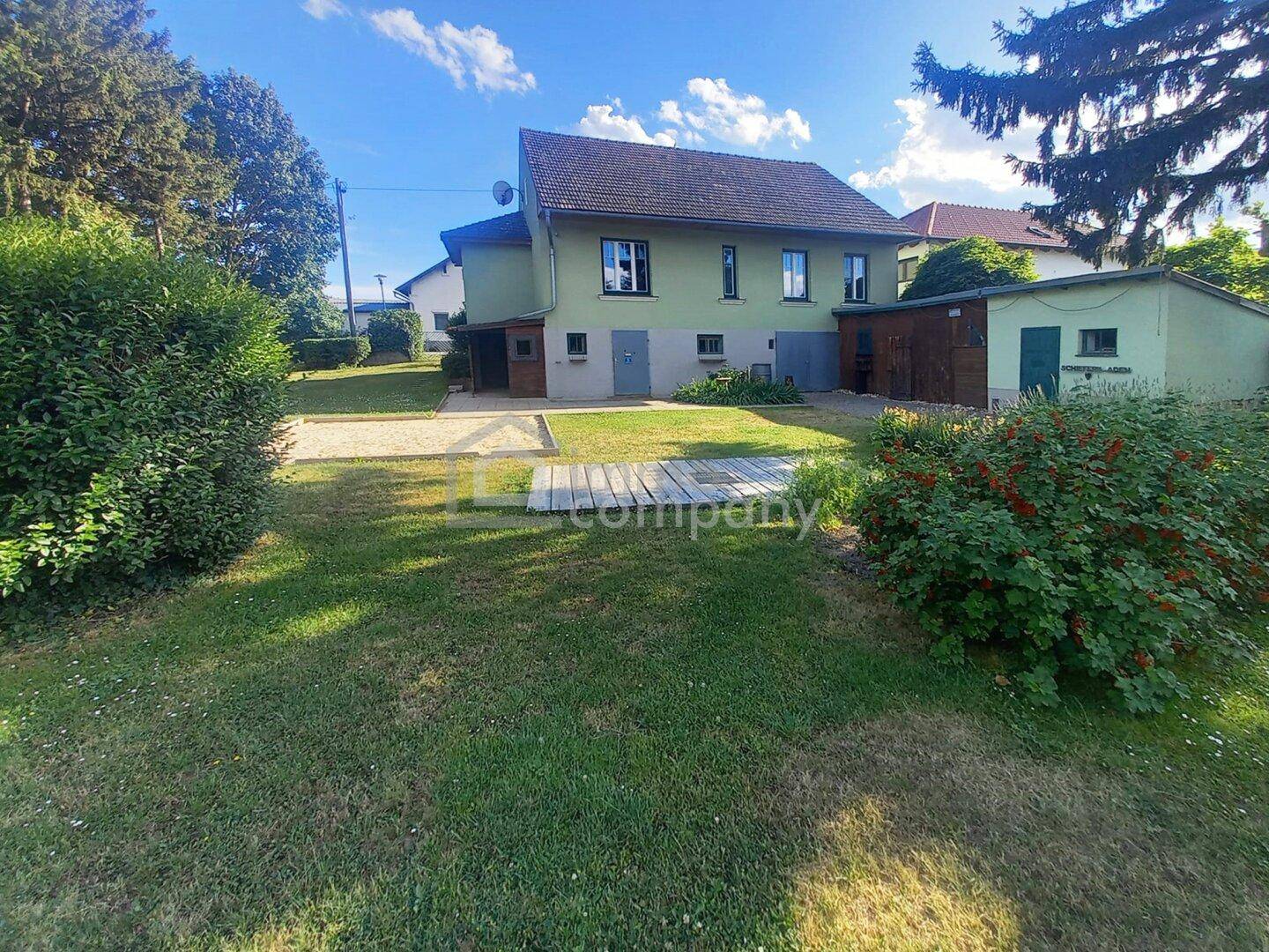 Hinterer Gartenbereich des Hauses mit Rasen, Holzschuppen und überdachtem Stellplatz.