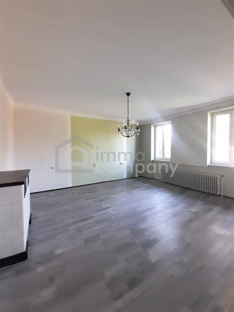 Helles Wohnzimmer mit grauem Laminatboden, hohen Decken und einem Kronleuchter.