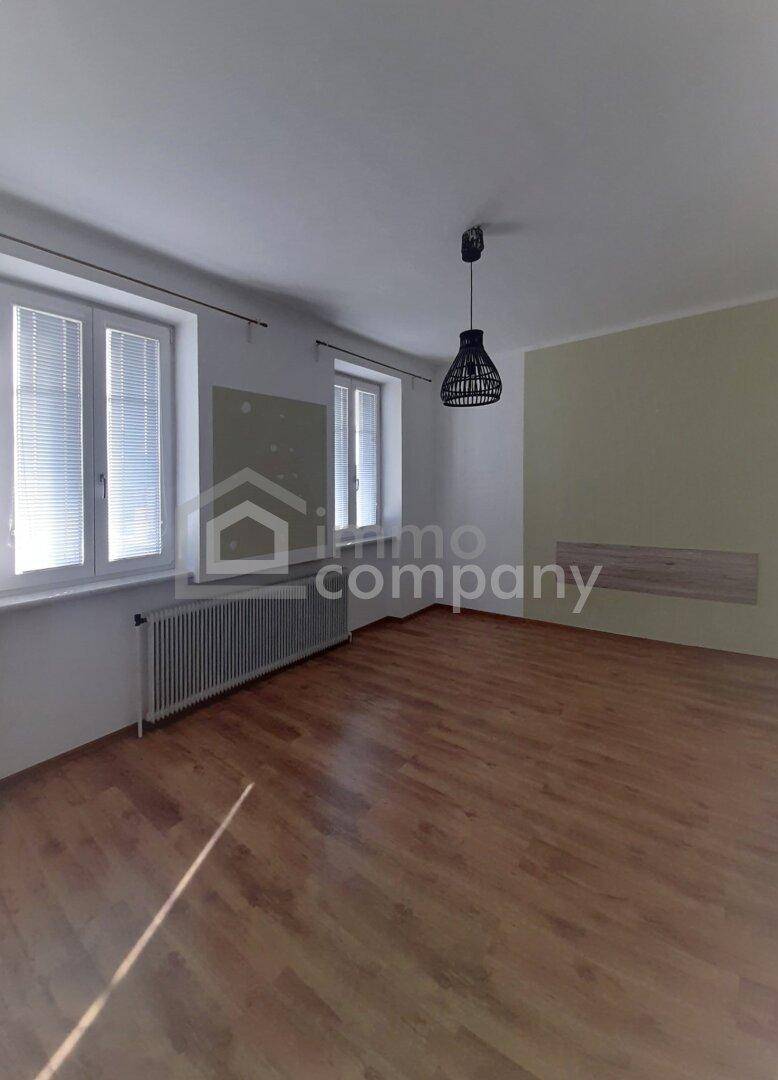 Heller Raum mit Holz-Laminatboden, zwei großen Fenstern und einem Heizkörper.