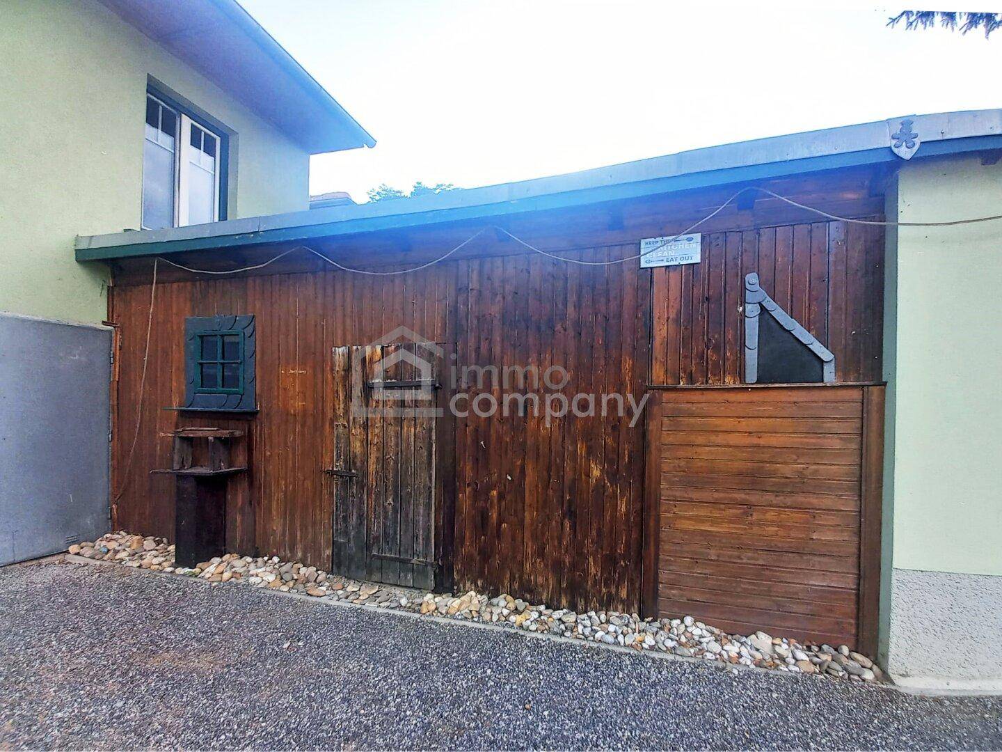 Rustikaler Holzschuppen neben dem Hauptgebäude mit kleiner Tür und Fenster.