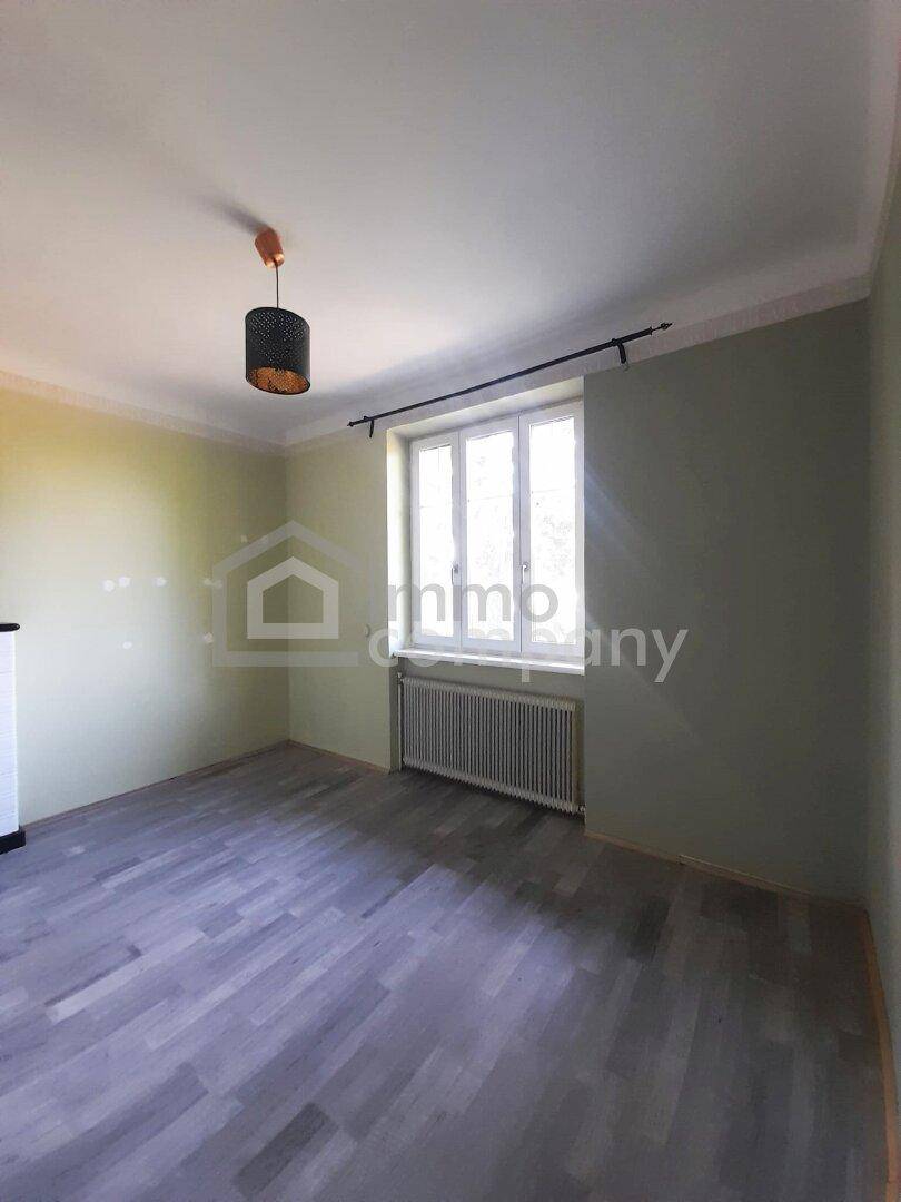 Leerer Raum mit grauem Laminatboden, einem großen Fenster und einem Heizkörper.