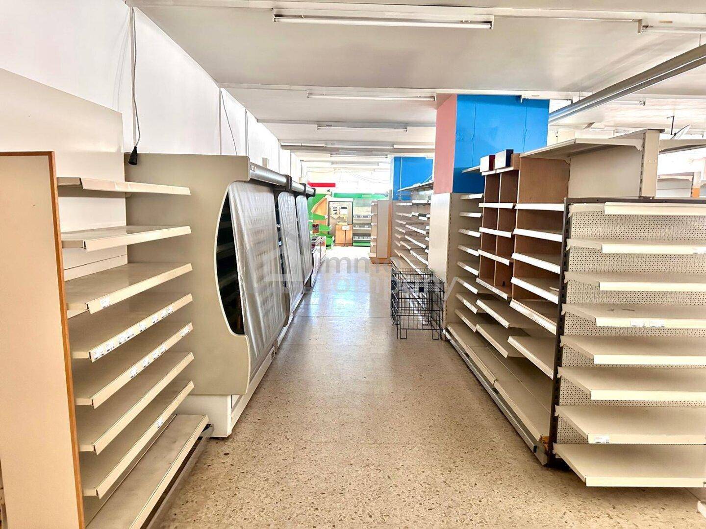Gang in einem leeren Supermarkt mit Kühlregalen und Terrazzoboden, gut beleuchtet.