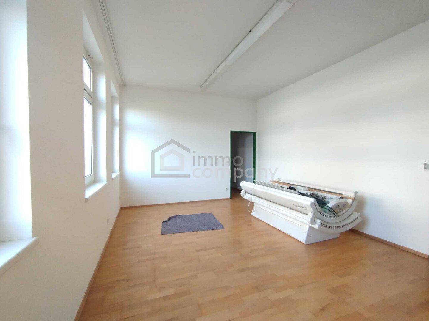 Heller Raum mit Holzboden, großen Fenstern und einem Solarium, ideal für ein Geschäft oder Studio.