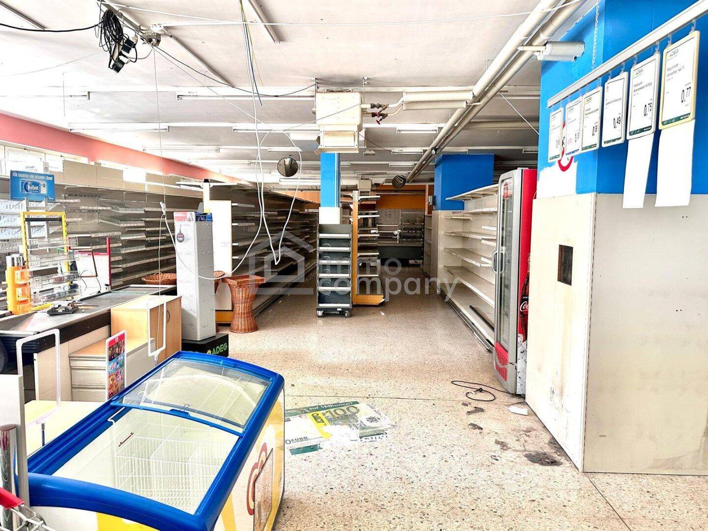 Verkaufsraum mit leeren Regalen, Kasse und Gefriertruhe, bereit zur Neugestaltung und Nutzung.