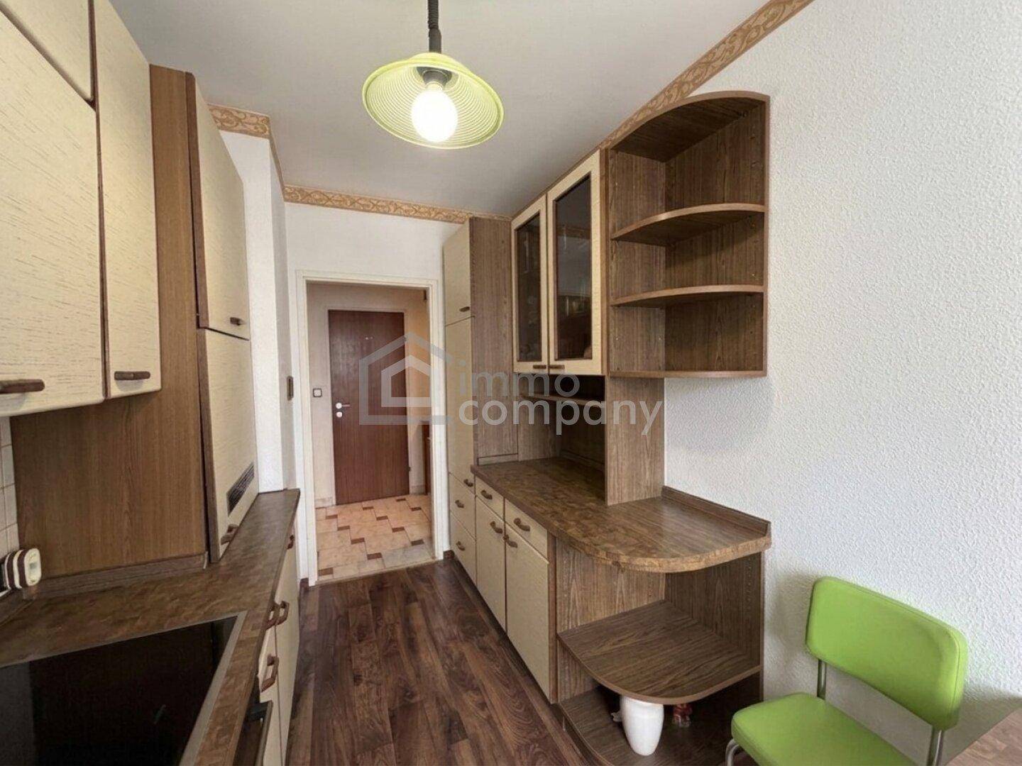 Küche mit Holzschränken, integrierten Regalen und einem kleinen Essbereich, hell beleuchtet.