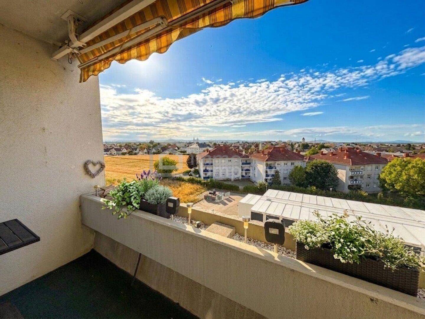 Sonniger Balkon mit Markise, Pflanzen und weitem Blick über die Landschaft und Dächer.