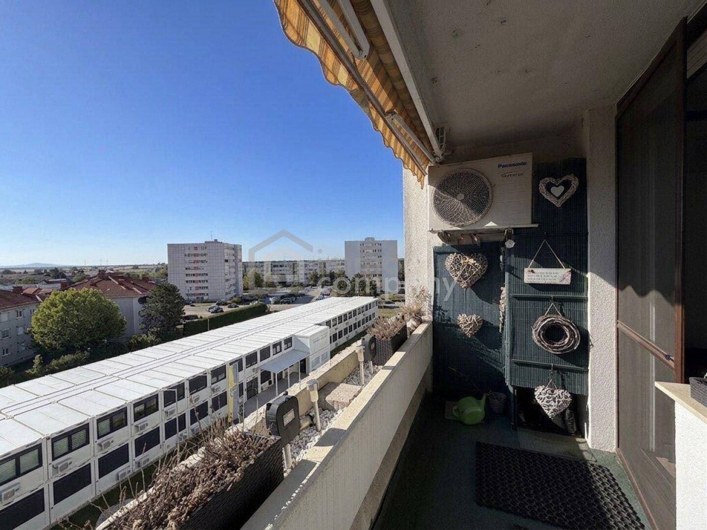 Balkon mit Klimaanlage und Blick auf umliegende Gebäude und die weite Landschaft.