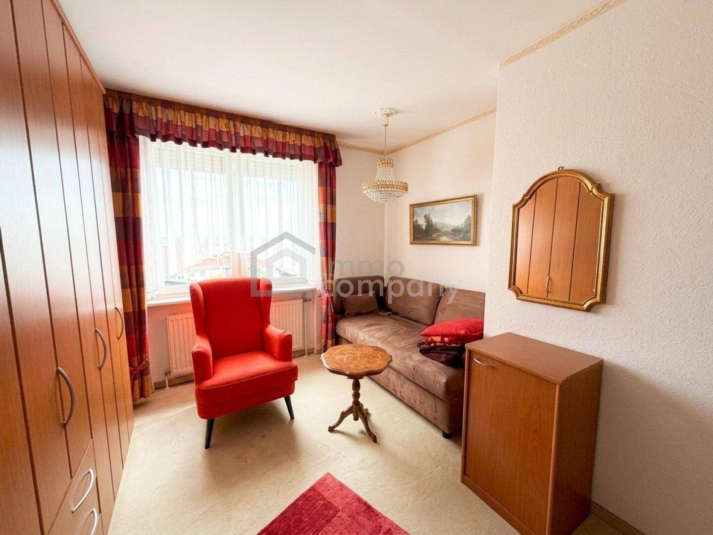 Helles Zimmer mit Einbauschränken, rotem Sessel und einem kleinen Tisch, gemütlich eingerichtet.
