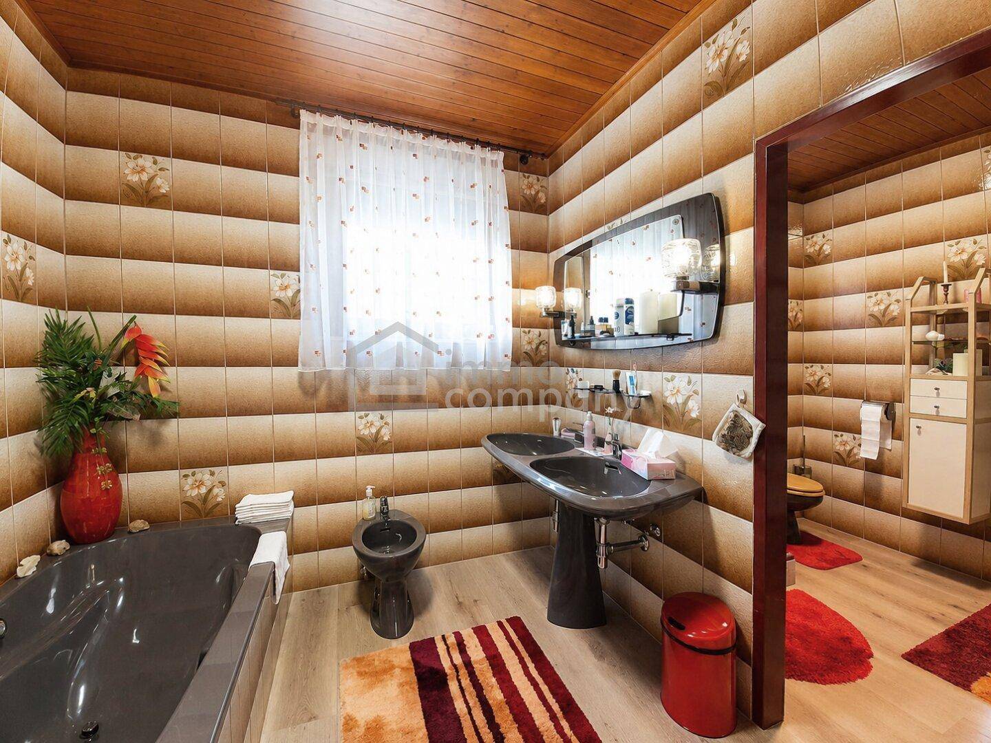 Badezimmer mit braun-beigen Fliesen, Doppelwaschbecken, Bidet und Badewanne.